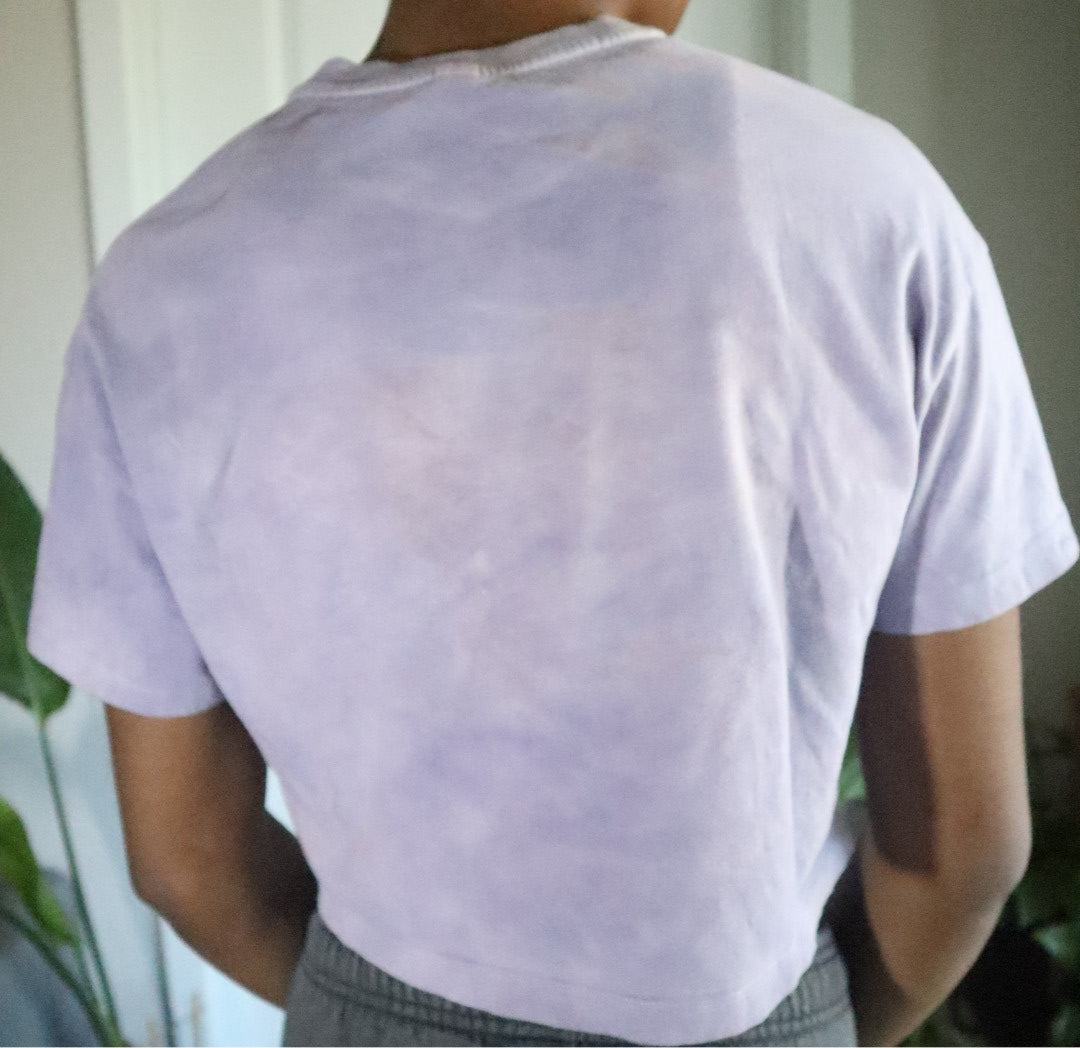 Person wearing a light purple t-shirt with visible stains, standing indoors.