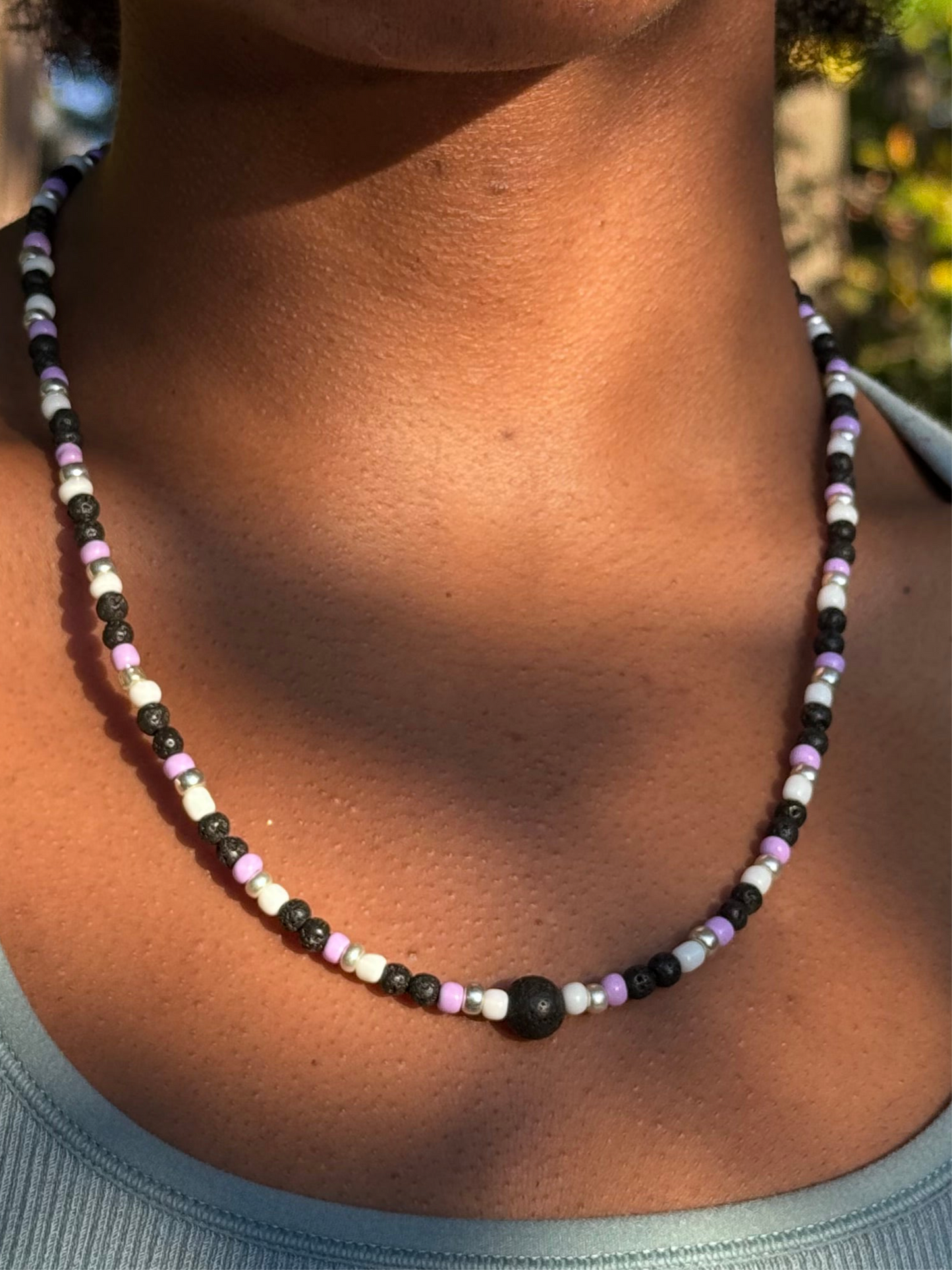 Close-up of a person wearing a beaded necklace with a blurred natural background