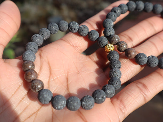 Hand holding a bracelet with dark beads on a blurred natural background