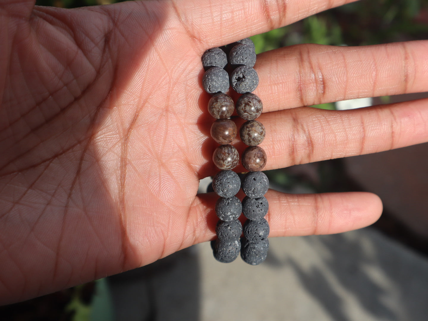 Hand holding a string of dark blue beads against a blurred natural background