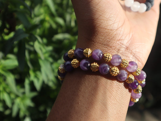 Purple beaded bracelet with gold accents on a wrist against a blurred green background