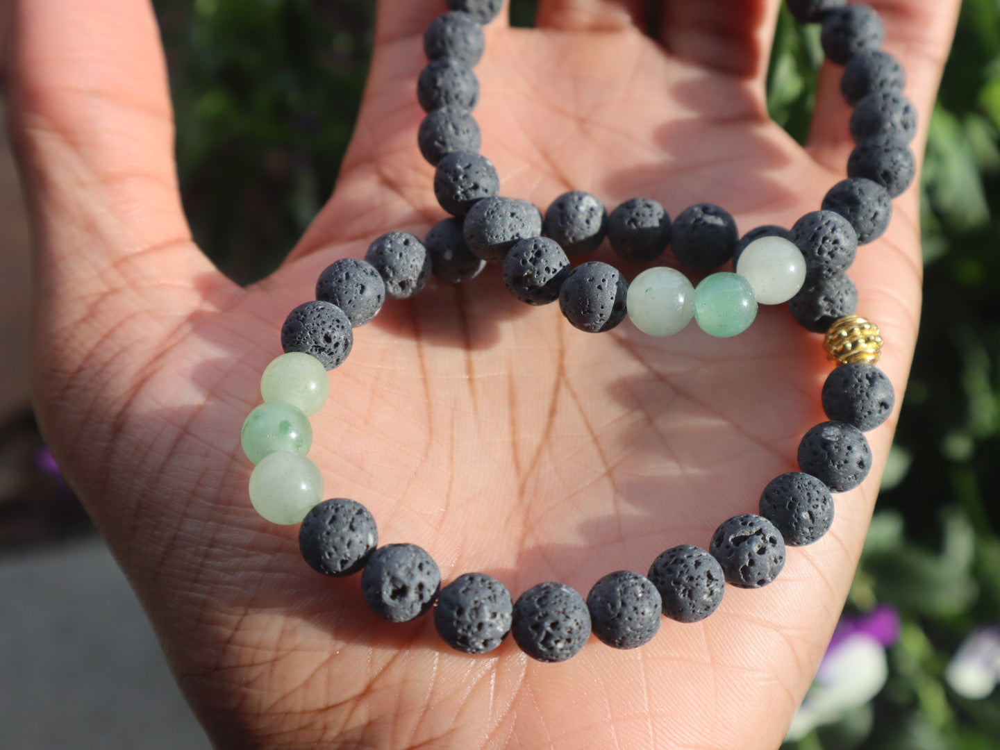 Lava stone and green bead bracelet on a hand with a blurred natural background