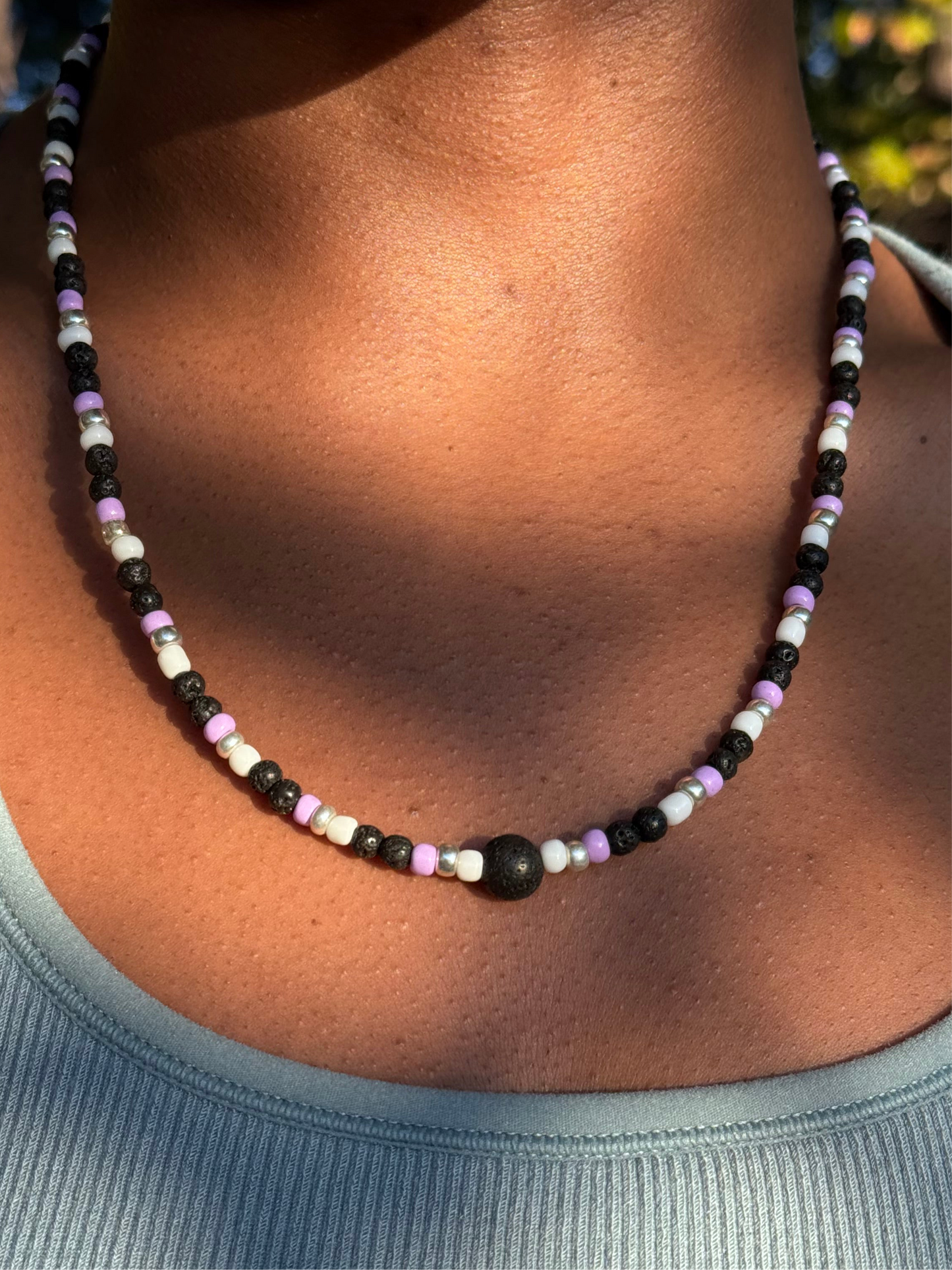 Necklace with black, white, and purple beads on a person wearing a light blue top.