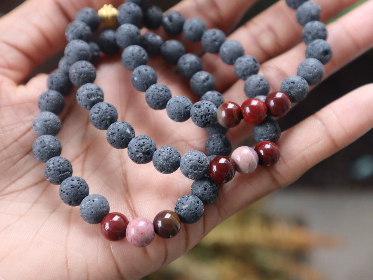 Hand holding a bracelet with red and pink beads.