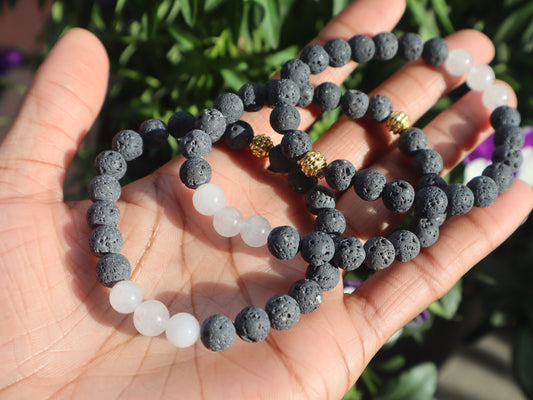 Hand holding two beaded bracelets with a blurred green background