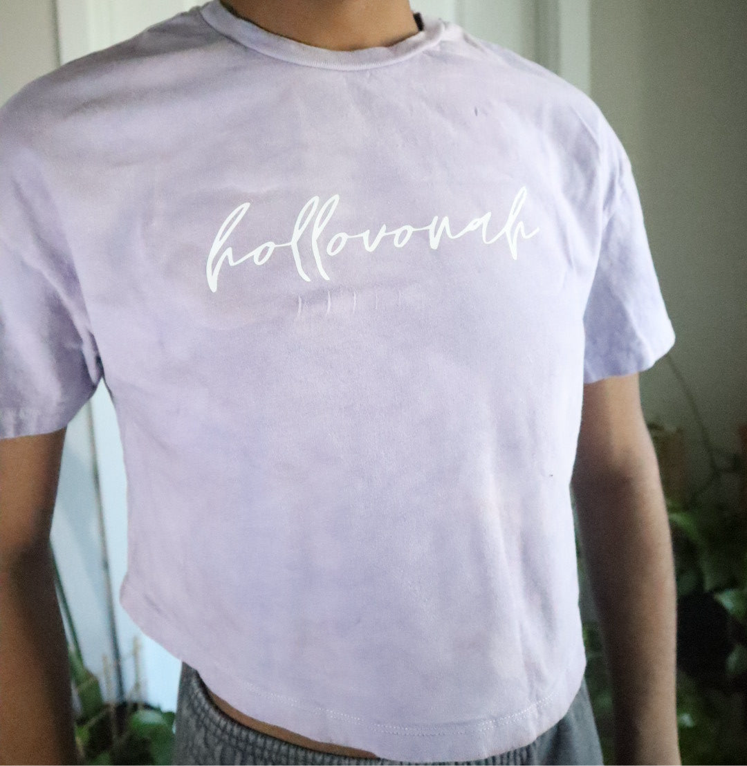 Person wearing a light purple t-shirt with 'hollovonah' printed on it, standing outdoors.
