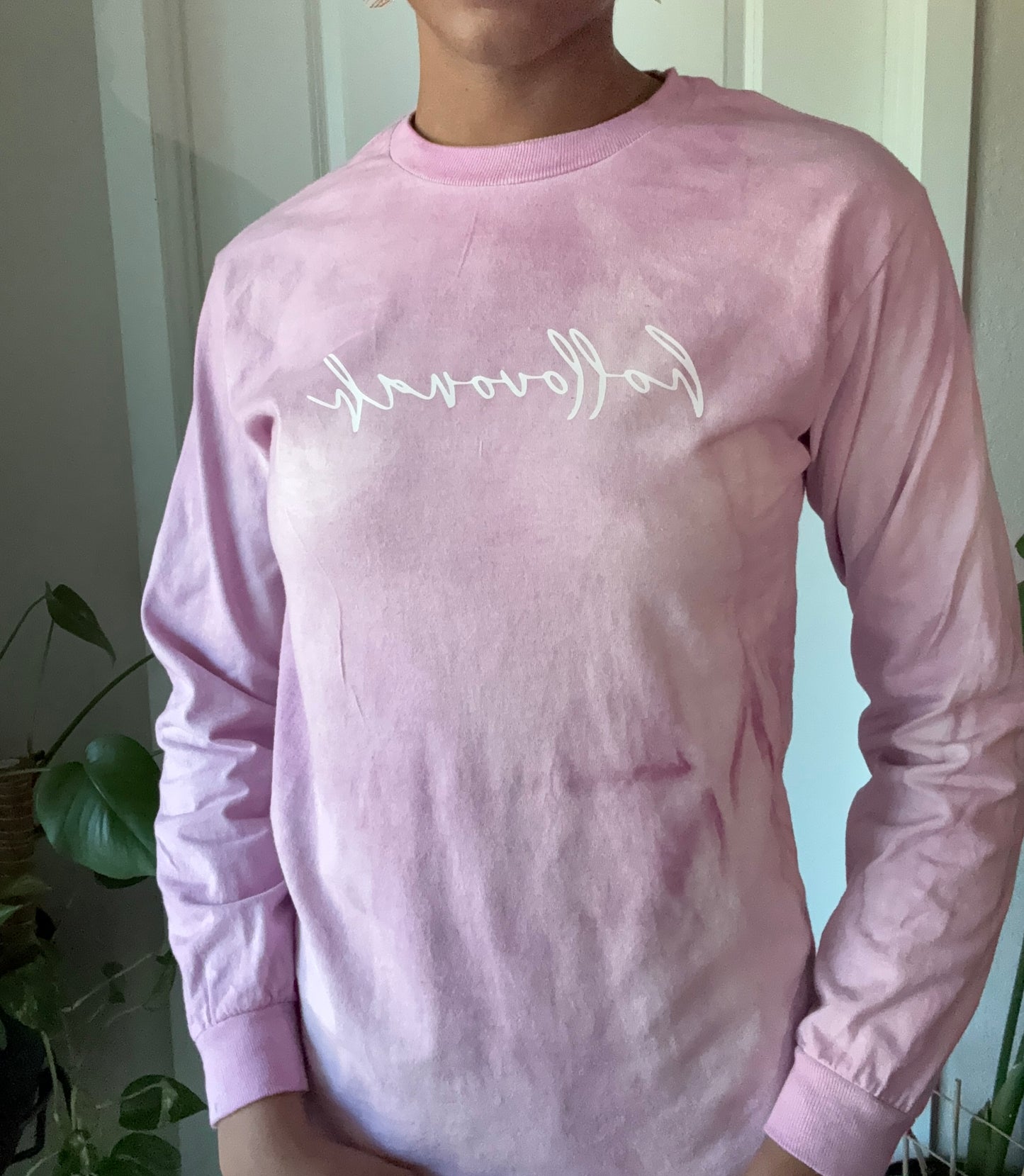 Person wearing a pink long-sleeve shirt with text, standing indoors.
