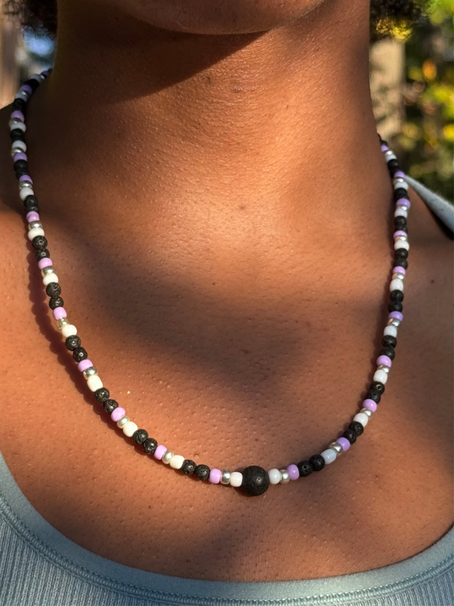 Close-up of a person wearing a beaded necklace with a blurred natural background