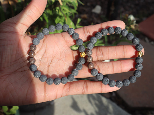 Hand holding two gray beaded bracelets with a blurred natural background