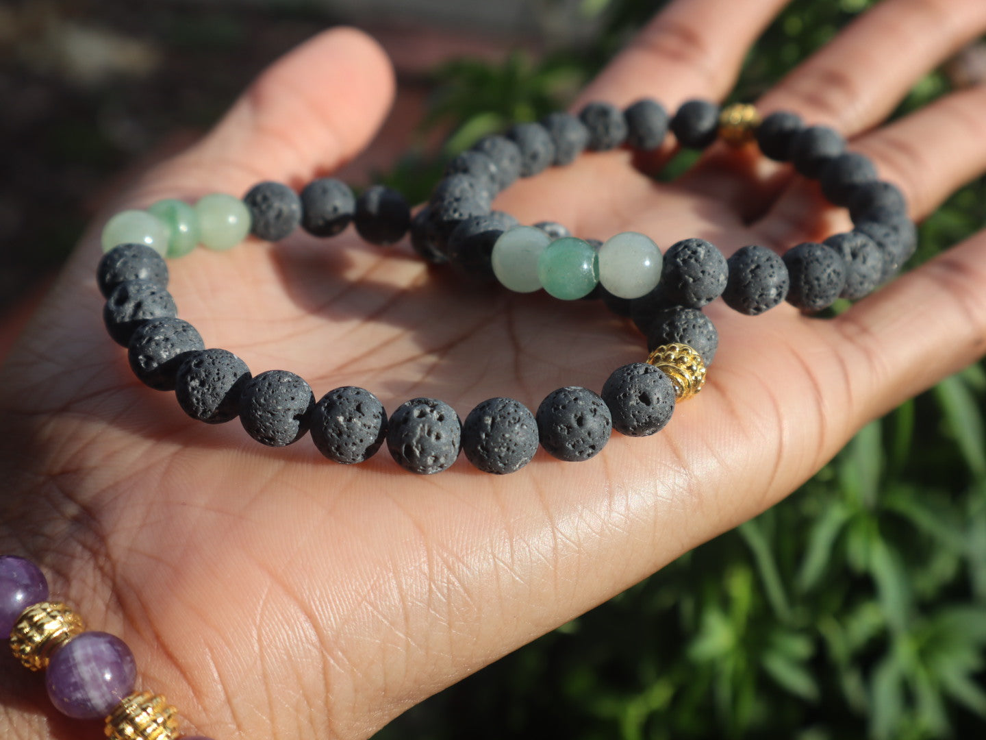 Hand holding a bracelet with black and green beads against a natural background