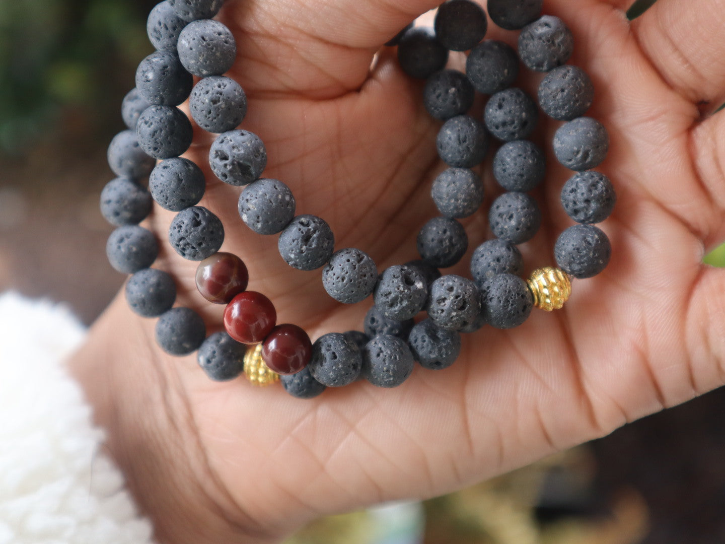 Hand holding a stack of dark gray beaded bracelets with gold and red accents.
