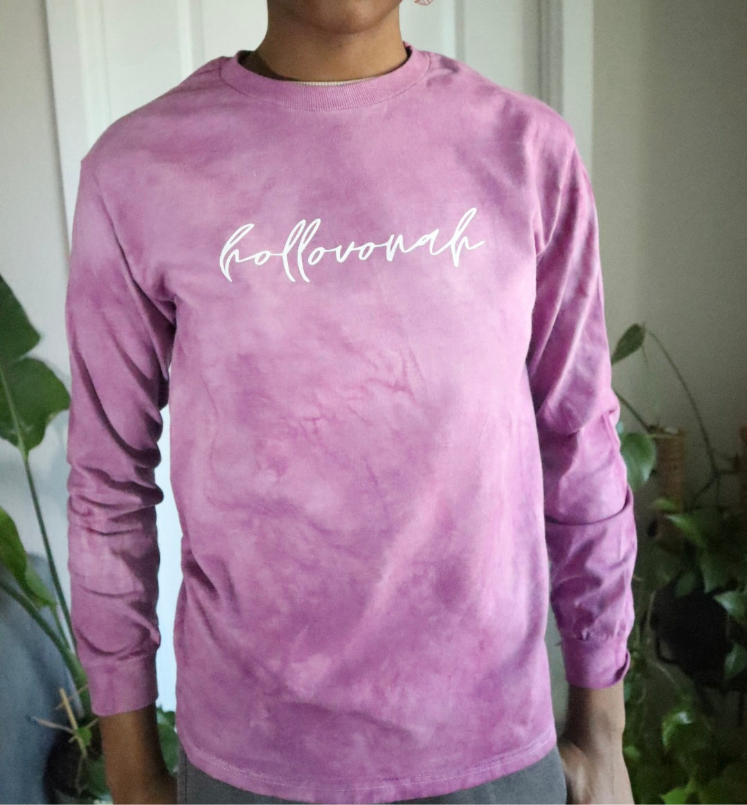 Person wearing a pink long-sleeve shirt with 'hollovonah' text, standing indoors with plants in the background.