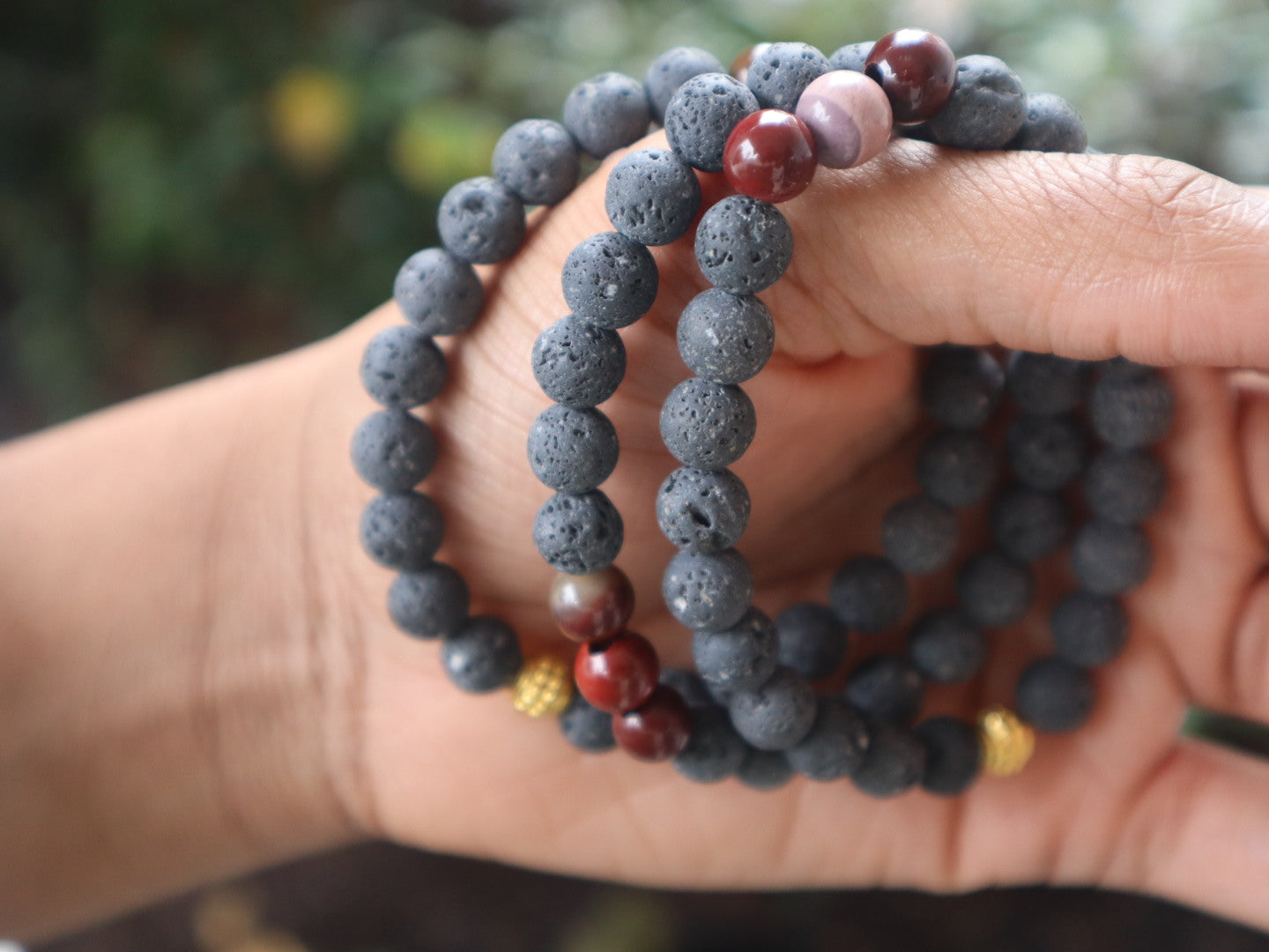Hand wearing two beaded bracelets with a blurred natural background