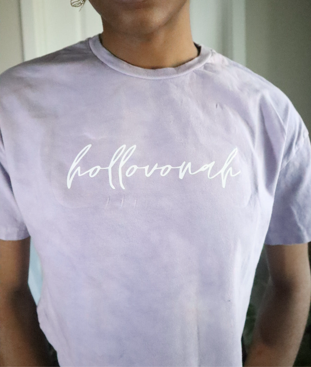 Person wearing a light purple t-shirt with 'hollovonah' printed on it.