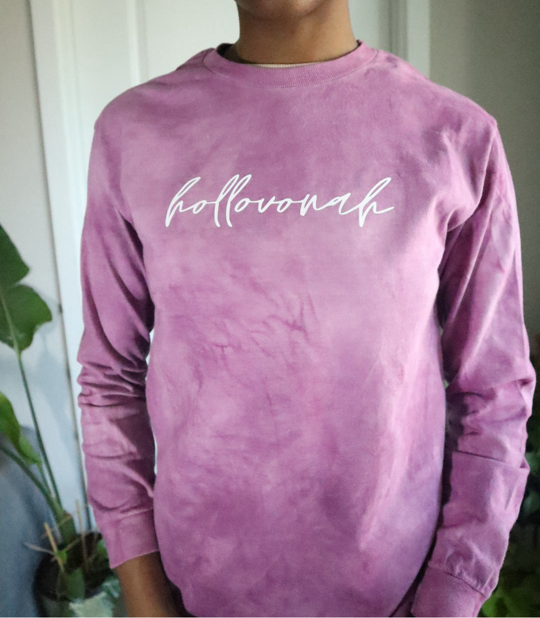Person wearing a pink long-sleeve shirt with 'hollovonah' text, standing indoors.