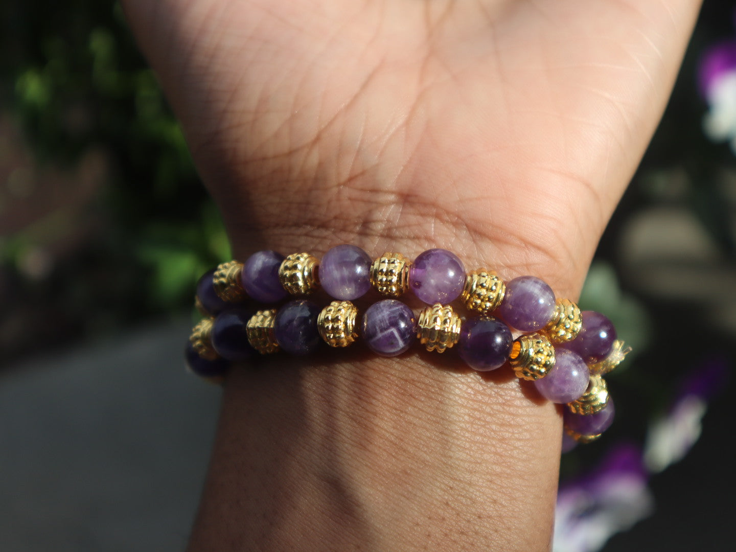 Purple beaded bracelet with gold accents on a wrist against a blurred background