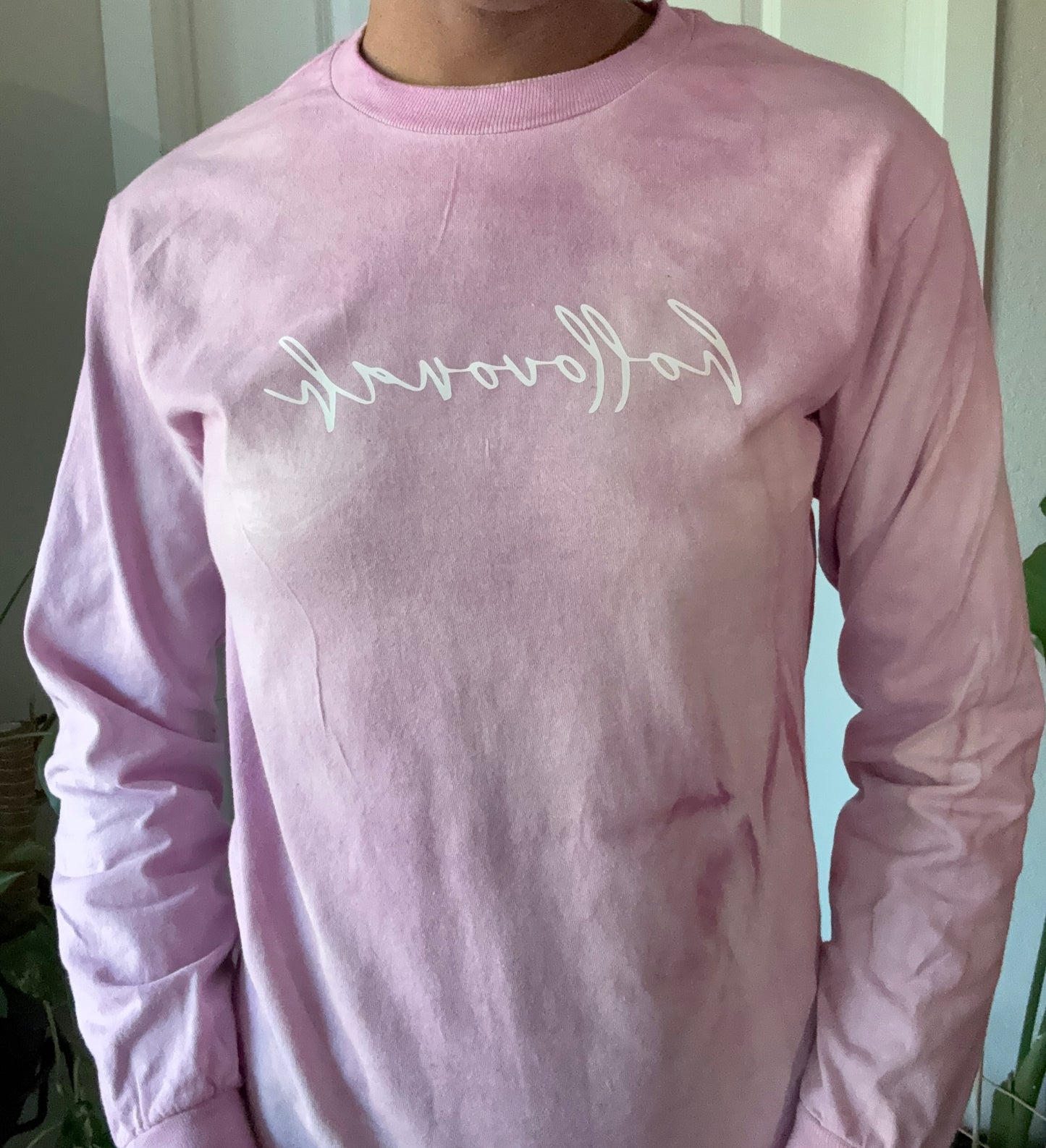 Pink long-sleeve shirt with white text worn by a person indoors.
