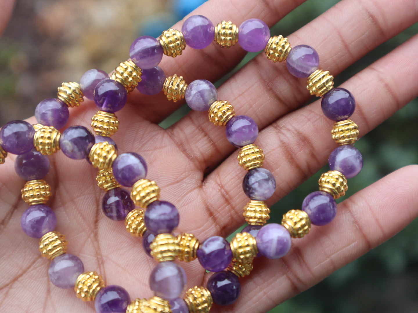 Purple beaded bracelet with gold accents on a hand against a blurred natural background