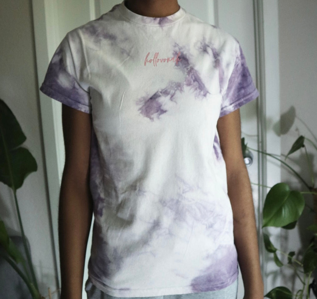 Person wearing a tie-dye t-shirt with purple and white patterns in a casual setting.