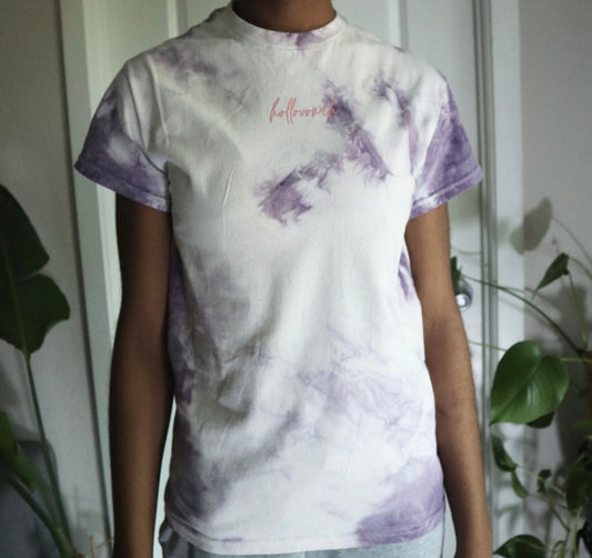 Person wearing a tie-dye t-shirt with purple and white patterns in a casual setting.