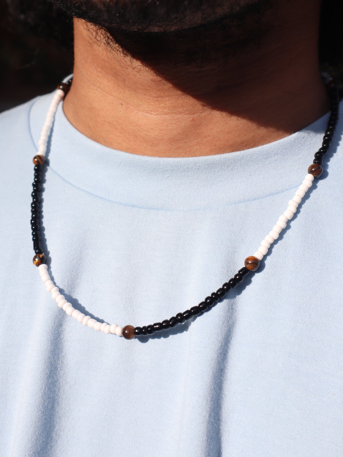 Close-up of a beaded necklace with white cord and brown beads on a light blue background.