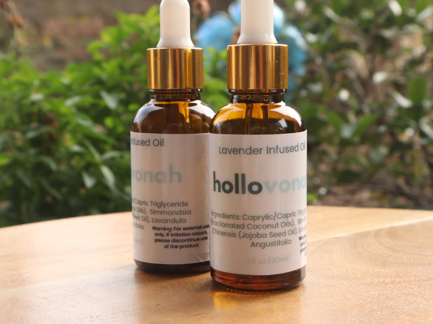 Two bottles of hollovan lavender infused oil on a wooden surface with a blurred green background.