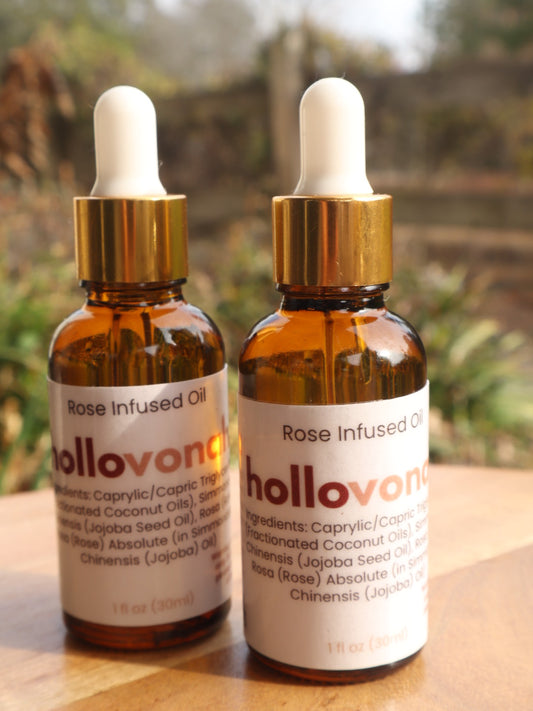 Two bottles of Holloway Rose Infused Oil on a wooden surface with a blurred natural background.