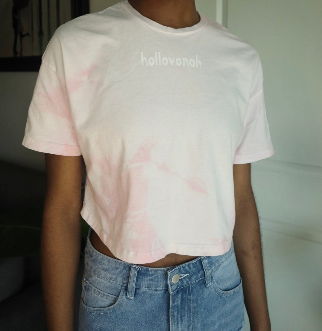 Person wearing a light pink tie-dye t-shirt with 'hollovonah' text and blue jeans.