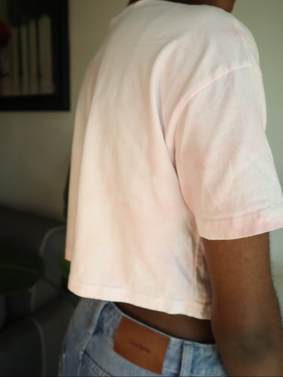 Person wearing a light pink tie-dye t-shirt and blue jeans with a brown belt.