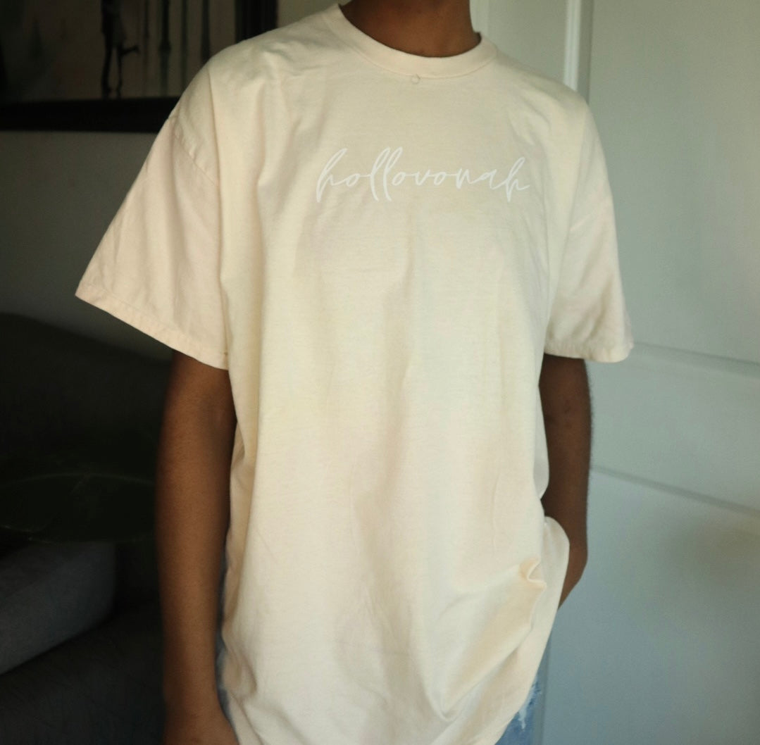 Person wearing a beige t-shirt with 'hollovonah' printed on it, standing indoors.