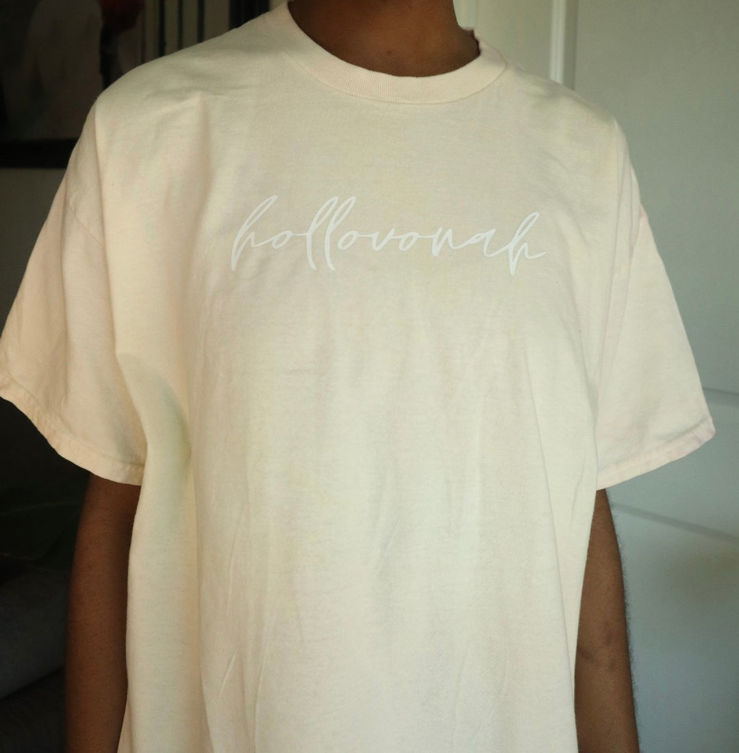 Beige t-shirt with 'hollovonah' text worn by a person indoors.