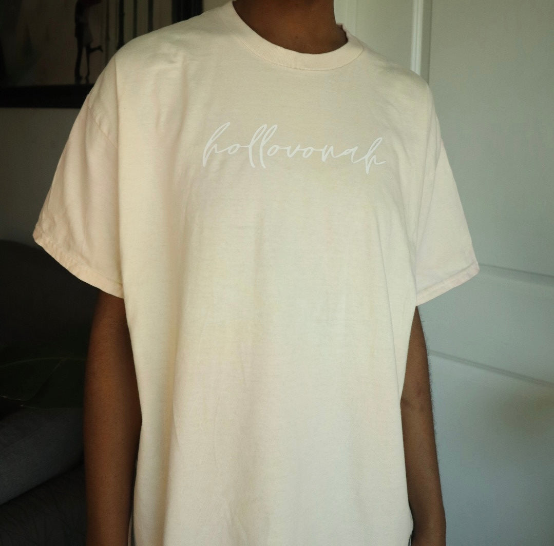 Person wearing a beige t-shirt with 'hollovonah' text in a neutral indoor setting