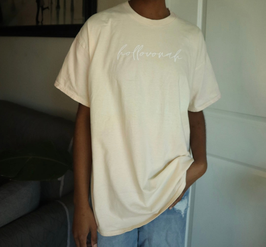 Person wearing a beige t-shirt with 'hollovonah' text in a casual setting